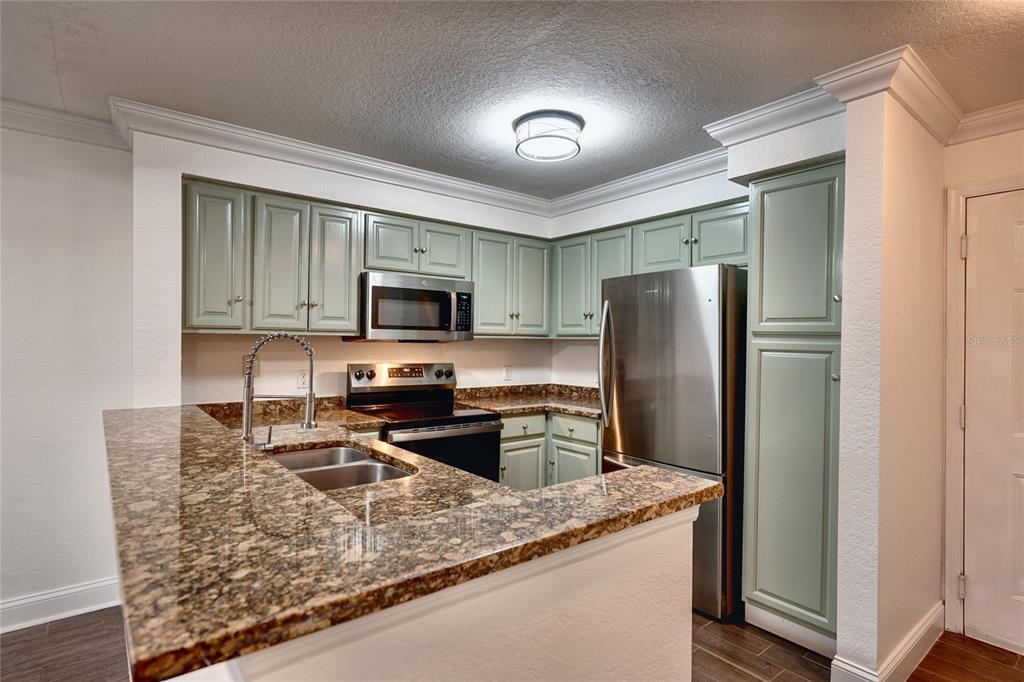 A kitchen features sage green cabinets, granite countertops, stainless steel appliances, and a breakfast bar — 13815 FAIRWAY ISLAND DRIVE UNIT 1335, ORLANDO, FL