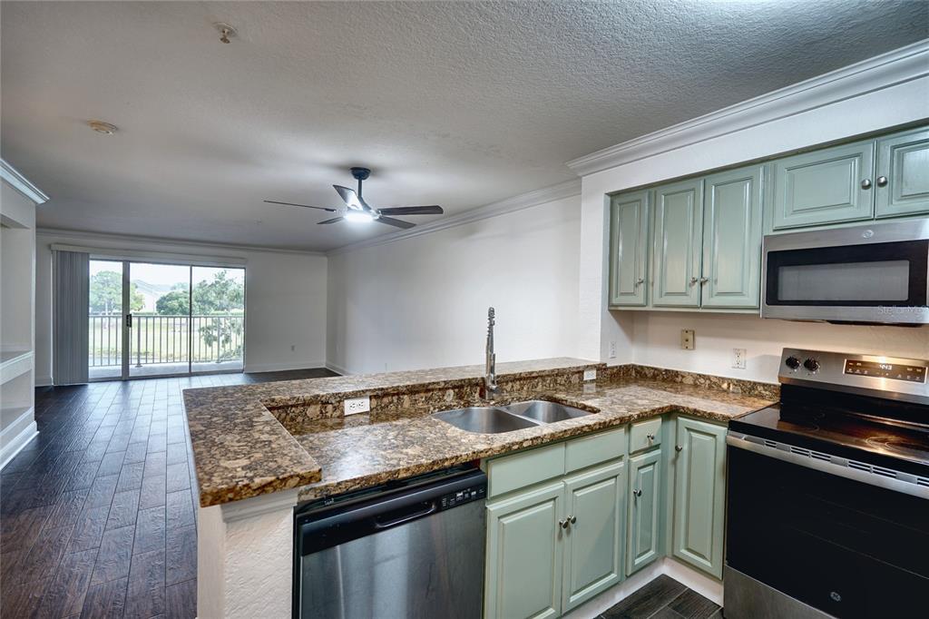 A kitchen with green cabinets, granite countertops, and stainless steel appliances overlooks a living area — 13815 FAIRWAY ISLAND DRIVE UNIT 1335, ORLANDO, FL