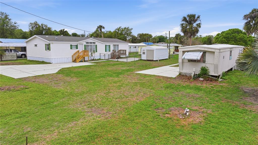 A white manufactured home and a smaller trailer sit on a grassy lot with sheds — 11923 SW LOOP TERRACE, ARCADIA, FL