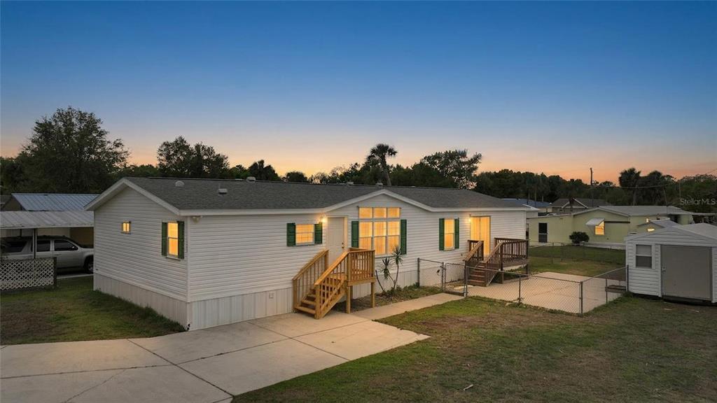 A white manufactured home with wooden stairs and a fenced yard at sunset — 11923 SW LOOP TERRACE, ARCADIA, FL