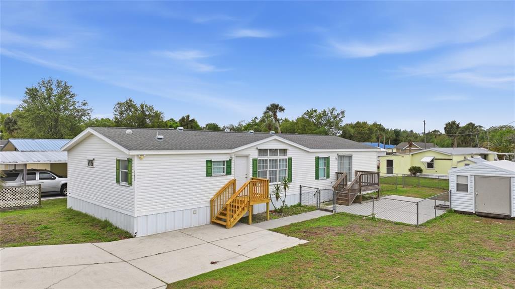 A white manufactured home with a concrete driveway, wooden stairs, and a small storage shed — 11923 SW LOOP TERRACE, ARCADIA, FL