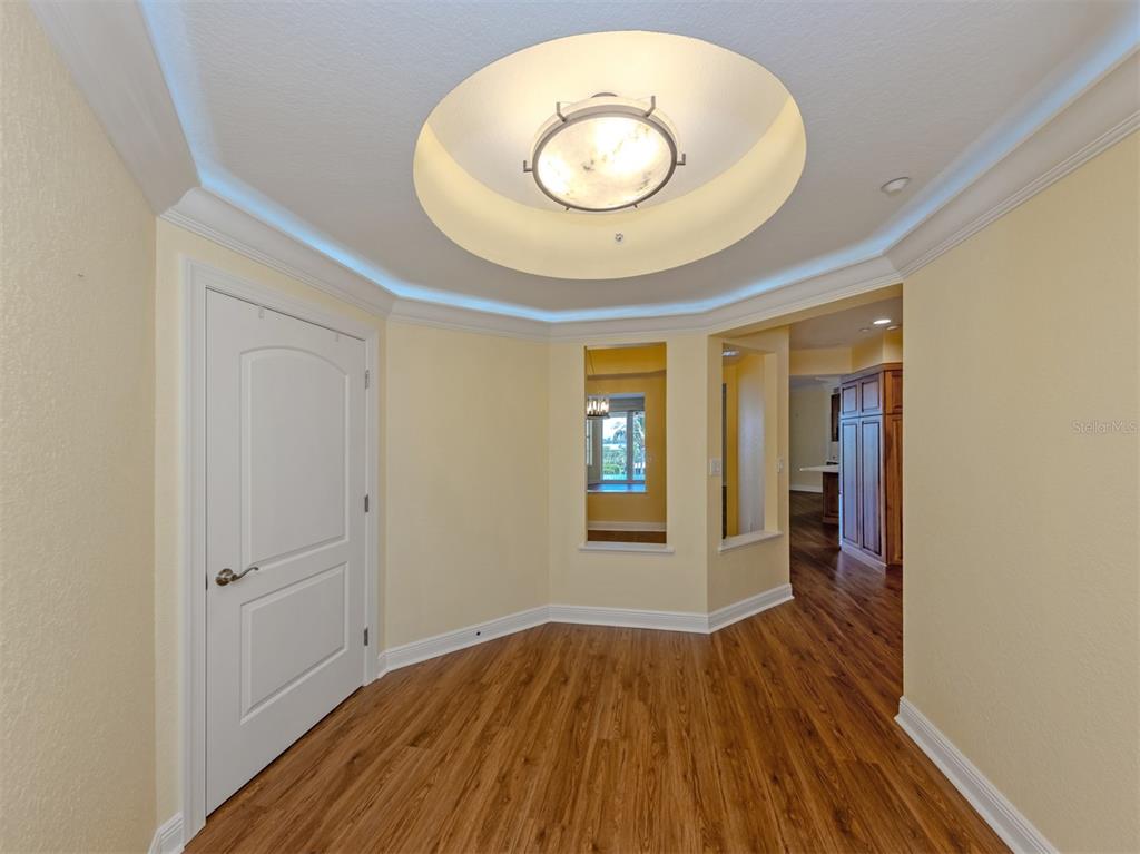 A foyer with wood-look flooring, a circular tray ceiling, and a view into a kitchen — 14021 BELLAGIO WAY UNIT 404, OSPREY, FL