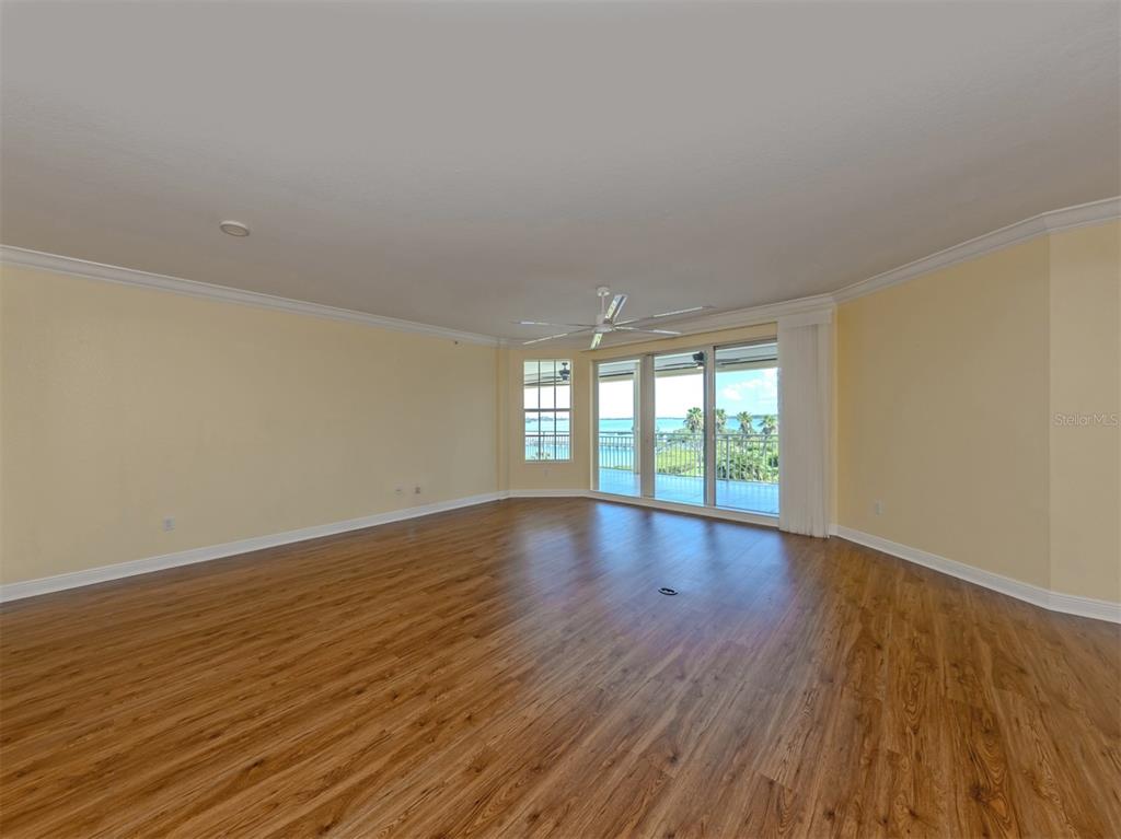 A spacious, empty living room with light yellow walls, wood-look flooring, and a balcony view — 14021 BELLAGIO WAY UNIT 404, OSPREY, FL
