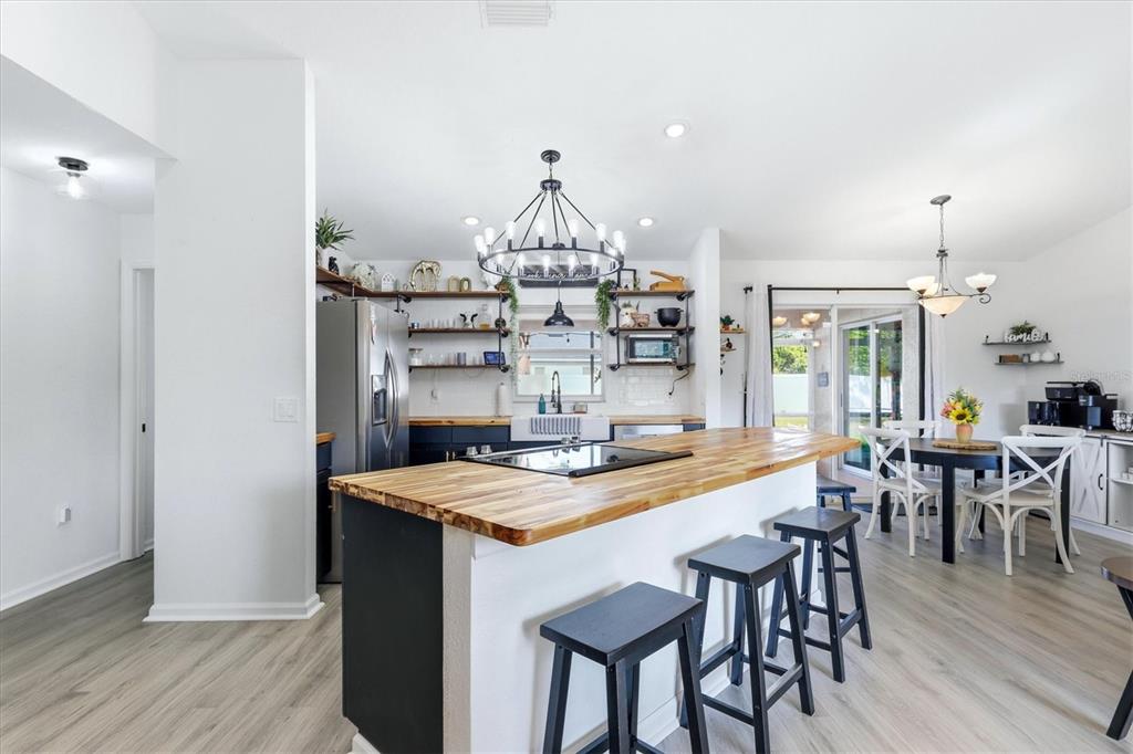 A kitchen with a wooden island, black bar stools, open shelving, and light wood flooring — 2565 CLOVELON STREET, NORTH PORT, FL