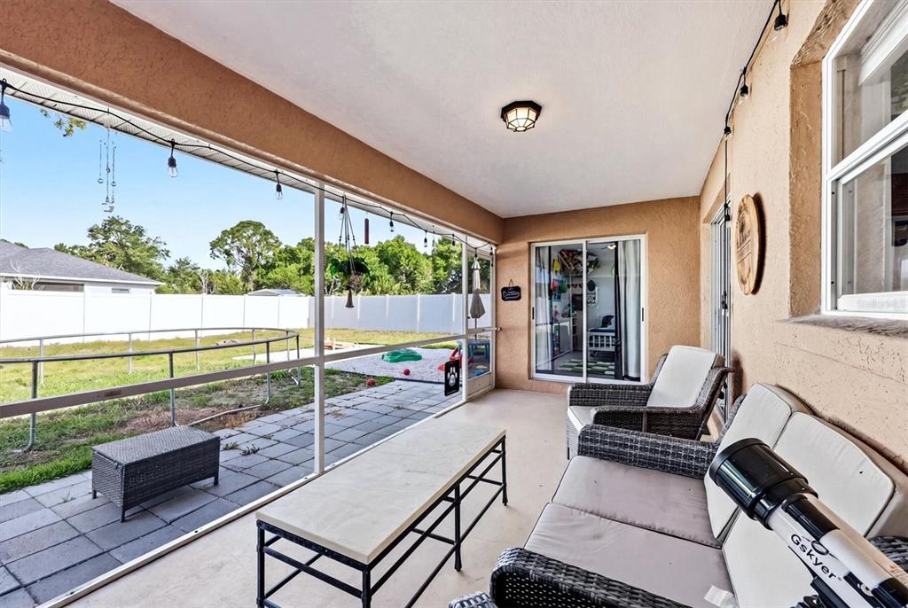 A screened-in patio features wicker furniture, a telescope, and a view of a fenced backyard — 2565 CLOVELON STREET, NORTH PORT, FL