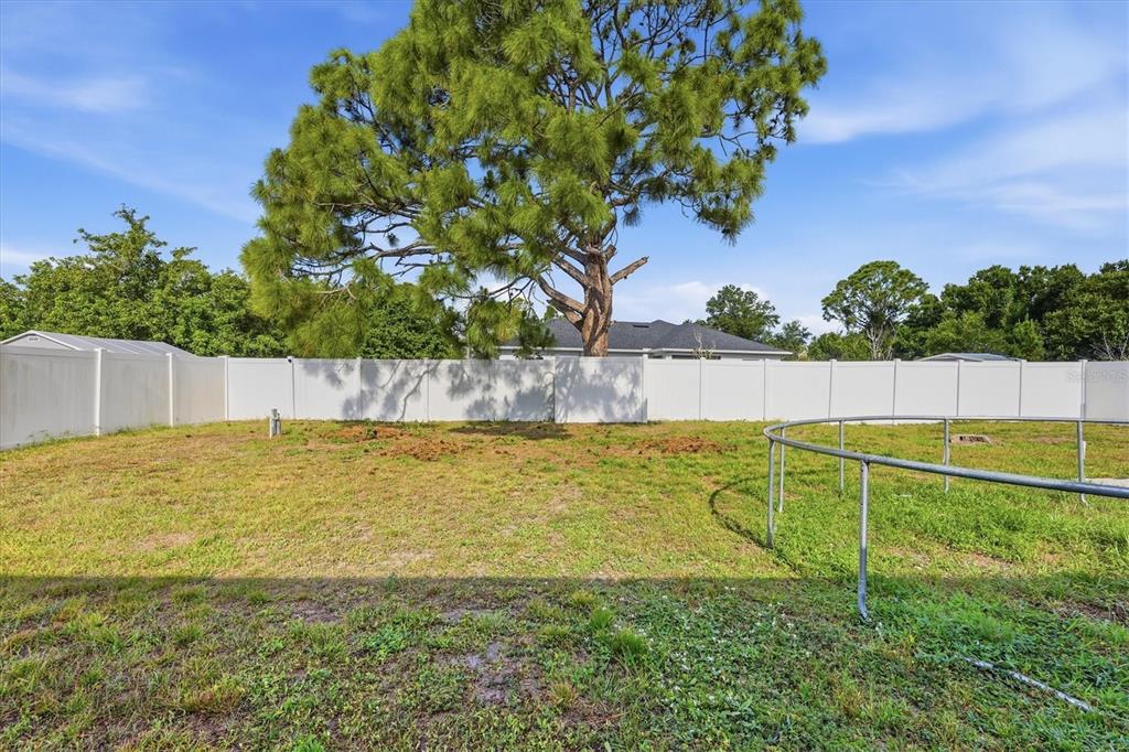 A grassy backyard features a large pine tree, a white vinyl fence, and a trampoline — 2565 CLOVELON STREET, NORTH PORT, FL