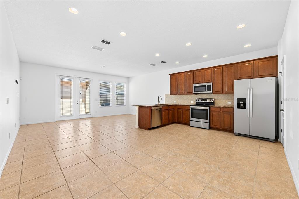 An open-concept kitchen and living area with tile flooring, wooden cabinets, and stainless steel appliances — 11429 BROWNSTONE STREET, WINDERMERE, FL