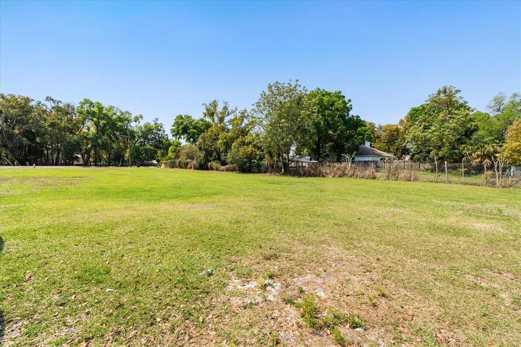 A wide, grassy vacant lot is bordered by mature trees and a residential fence — 28 REWIS STREET, OCOEE, FL