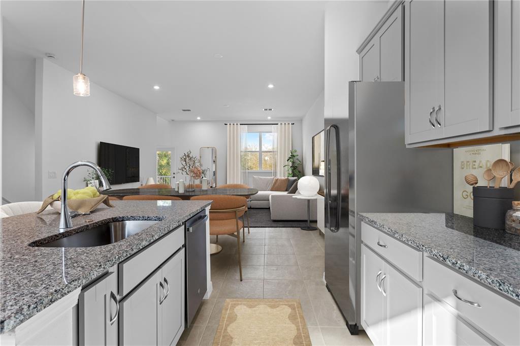 A kitchen with granite countertops and gray cabinets opens into a living and dining area — 9610 MONTAGUE STREET, WESTCHASE, FL
