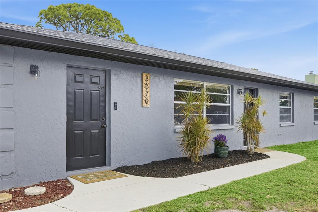 A gray exterior wall features a black front door, a window, and a vertical address plaque — 3670 SUNSET BEACH DRIVE, VENICE, FL