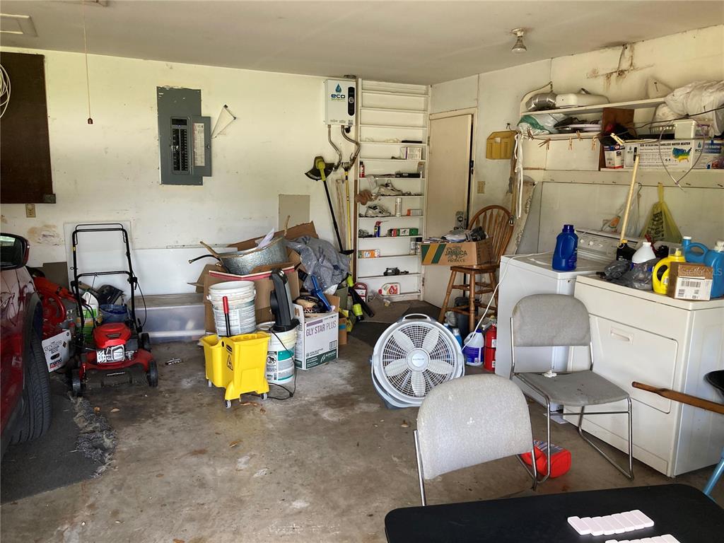 A cluttered garage contains a lawn mower, laundry appliances, shelving, and various household items — 2629 S PARSONS AVENUE, SEFFNER, FL