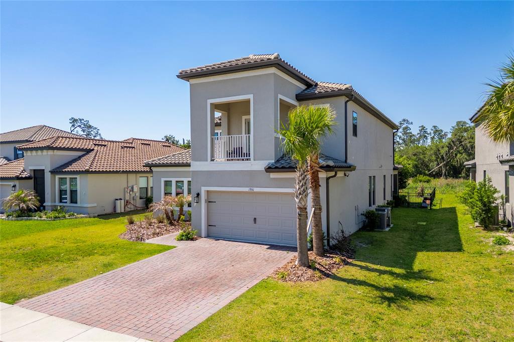 A two-story suburban house with a gray stucco exterior, a brick driveway, and a balcony — 1951 GOBLET COVE STREET, KISSIMMEE, FL