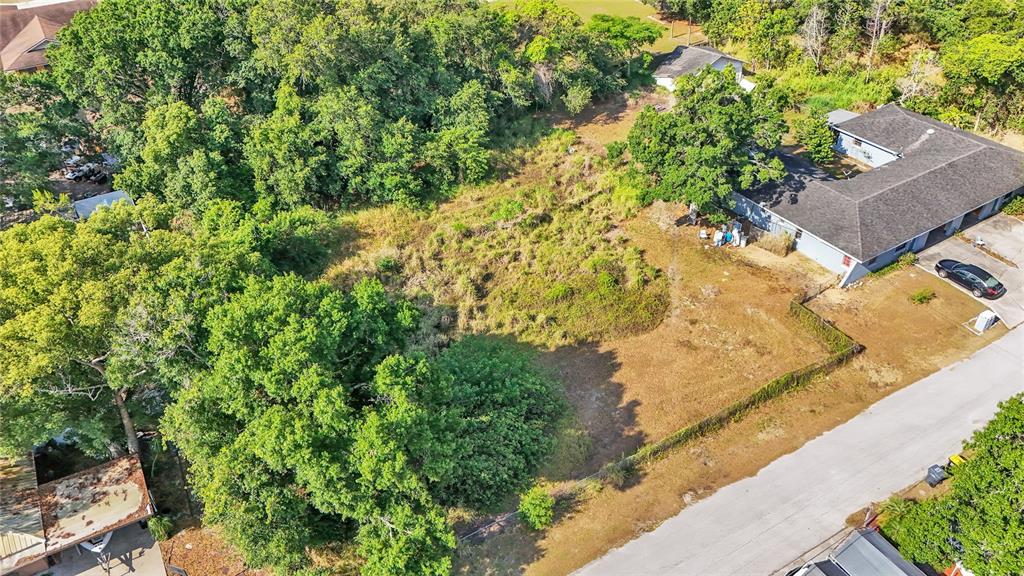 An aerial view shows a vacant, grassy lot situated between a residential building and trees — 1405 POLSTON ROAD, EAGLE LAKE, FL