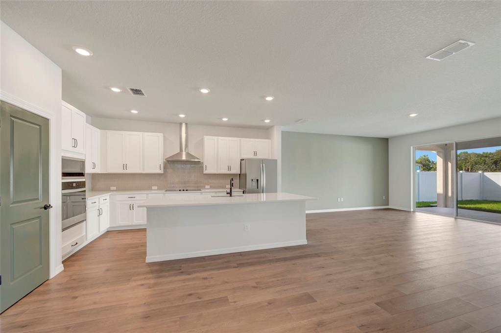 A modern kitchen with white cabinets, a central island, and wood-look flooring opens to a patio — 614 KINGSWOOD COURT, BRADENTON, FL