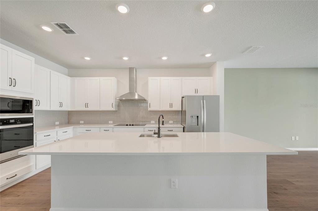 A modern kitchen features white cabinetry, a large central island, and stainless steel appliances — 614 KINGSWOOD COURT, BRADENTON, FL