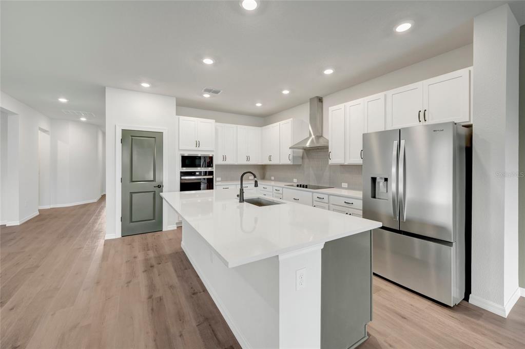 A modern kitchen features white cabinets, a large island with a sink, and stainless appliances — 614 KINGSWOOD COURT, BRADENTON, FL