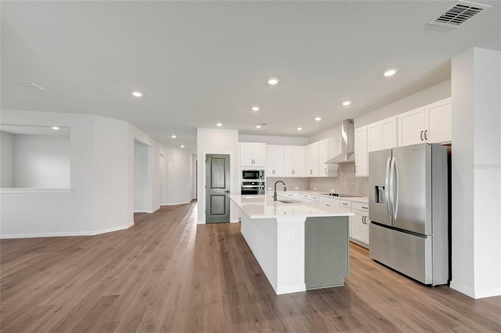 A modern kitchen features white cabinetry, a gray island, stainless steel appliances, and wood flooring — 614 KINGSWOOD COURT, BRADENTON, FL
