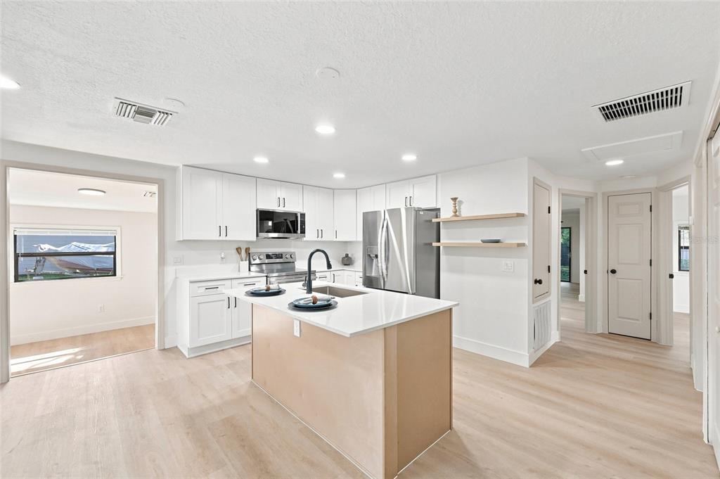 A modern kitchen features white cabinetry, a central island with a sink, and light wood flooring — 118 COURT STREET, KISSIMMEE, FL