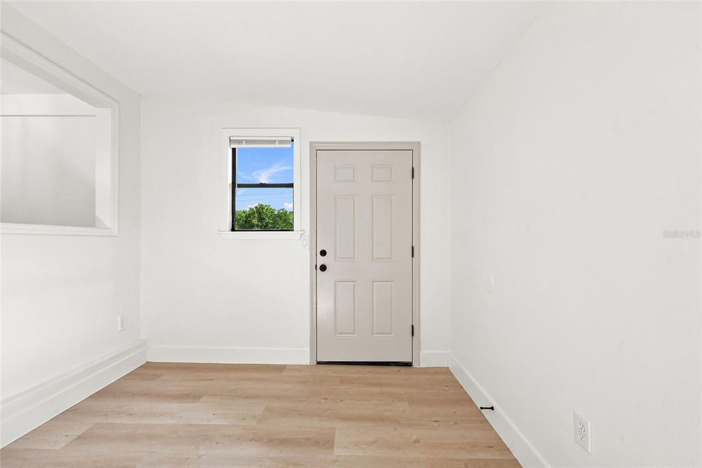 A room with white walls, light wood-look flooring, a single window, and a beige door — 118 COURT STREET, KISSIMMEE, FL