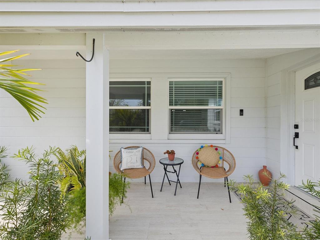 A covered front porch features two wicker chairs, a small table, and white siding — 10264 OAKHURST ROAD, LARGO, FL