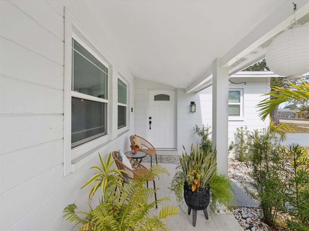 A white house exterior features a covered front porch with two chairs and potted plants — 10264 OAKHURST ROAD, LARGO, FL