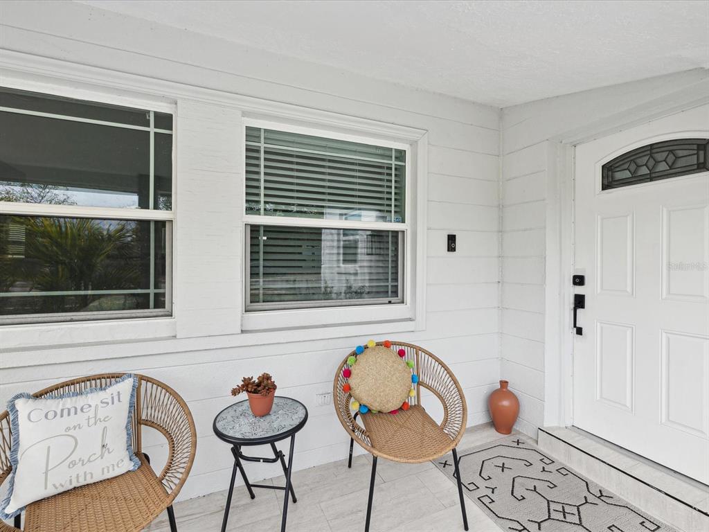 A white front porch features two wicker chairs, a small side table, and a front door — 10264 OAKHURST ROAD, LARGO, FL