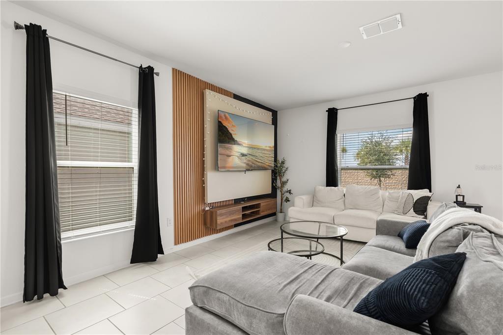 A living room features a wood-slat accent wall, a wall-mounted television, and two grey sofas — 368 LOCH COURT, DAVENPORT, FL