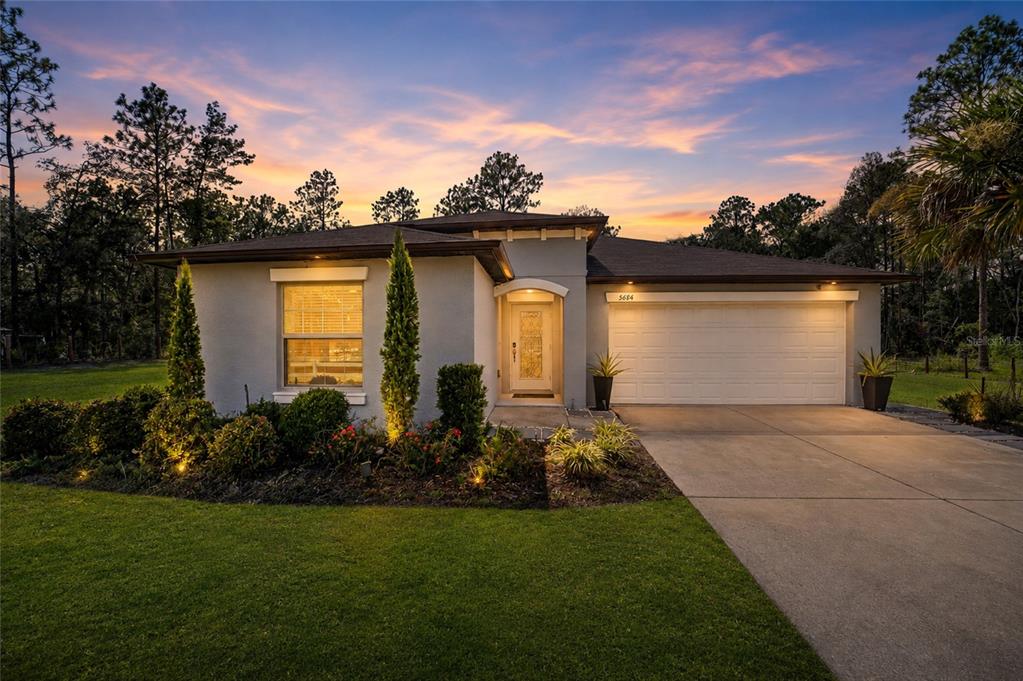 A single-story house with a two-car garage and landscaped front yard at sunset — 5684 SW 136TH AVENUE, OCALA, FL
