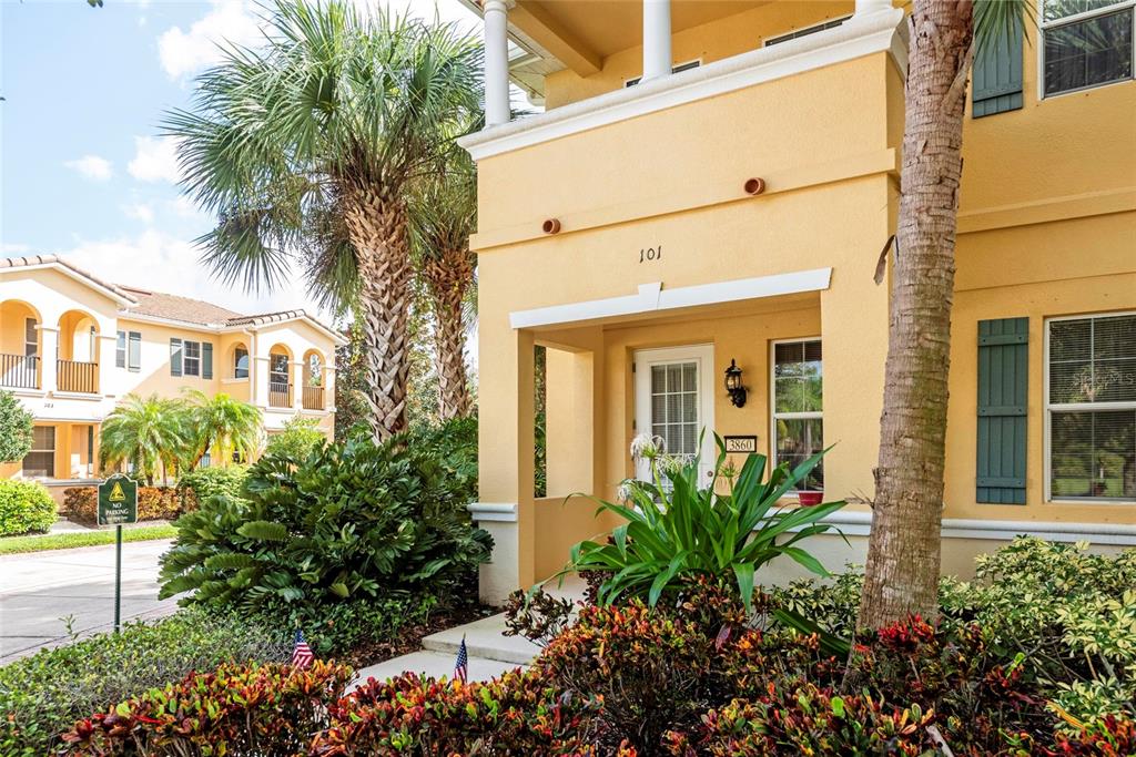 The exterior of a yellow two-story building features a covered entryway and lush landscaping — 3860 82ND AVENUE CIRCLE E UNIT 101, SARASOTA, FL