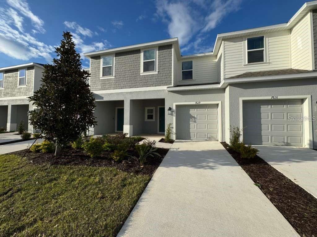 A two-story townhouse exterior features gray siding, a concrete driveway, and attached garages — 7629 WATERSCAPE DRIVE, GROVELAND, FL