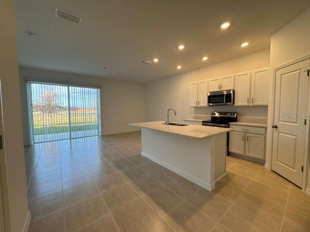 A kitchen with white cabinets, a central island, and tile flooring opens to a living area — 7629 WATERSCAPE DRIVE, GROVELAND, FL