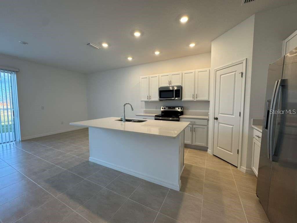 A modern kitchen features white cabinetry, a central island with a sink, and tile flooring — 7629 WATERSCAPE DRIVE, GROVELAND, FL