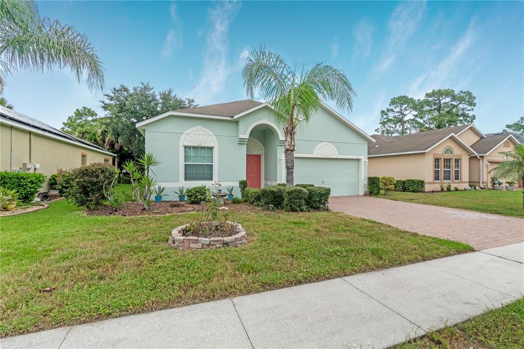 A light green single-story house features a red front door and a paved driveway — 3923 SUNSET COVE DRIVE, PORT ORANGE, FL