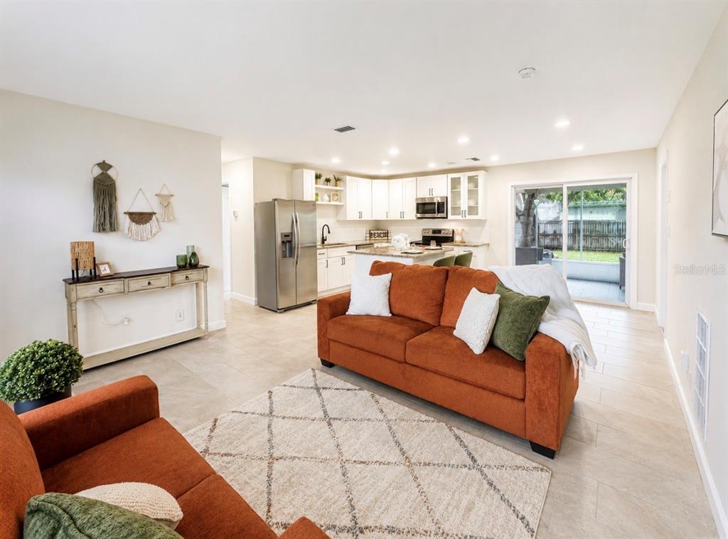 A living room with orange sofas and a rug opens into a kitchen with white cabinets — 482 OAKWOOD DRIVE, DUNEDIN, FL
