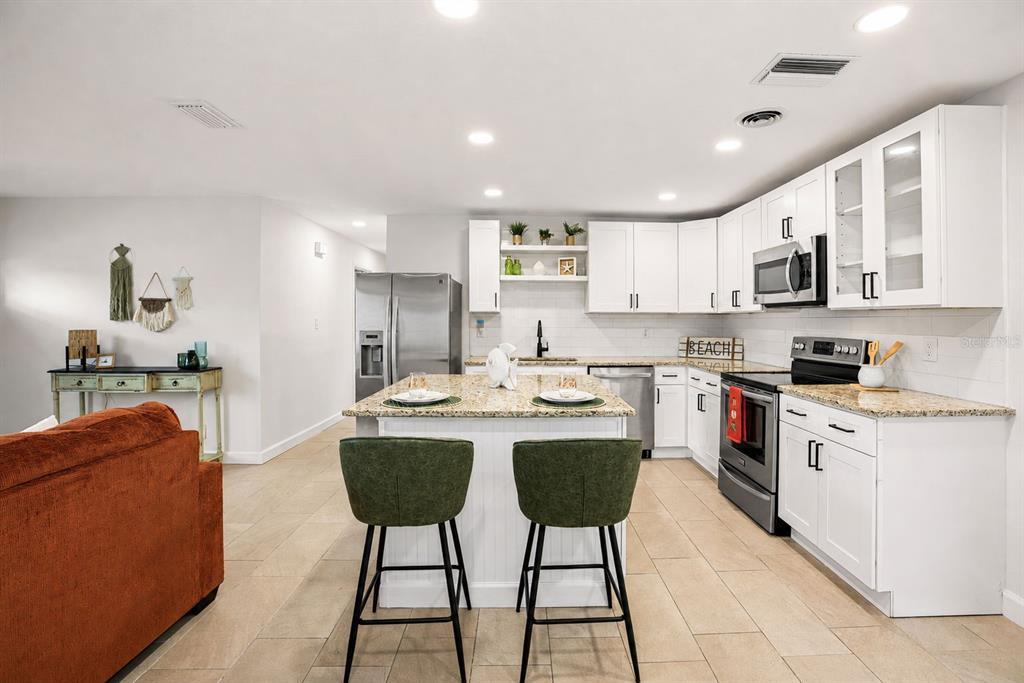 A kitchen with white cabinets, granite countertops, a center island, and two green bar stools — 482 OAKWOOD DRIVE, DUNEDIN, FL
