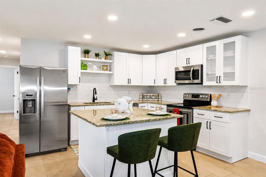 A kitchen with white cabinets, granite countertops, a center island, and two green bar stools — 482 OAKWOOD DRIVE, DUNEDIN, FL