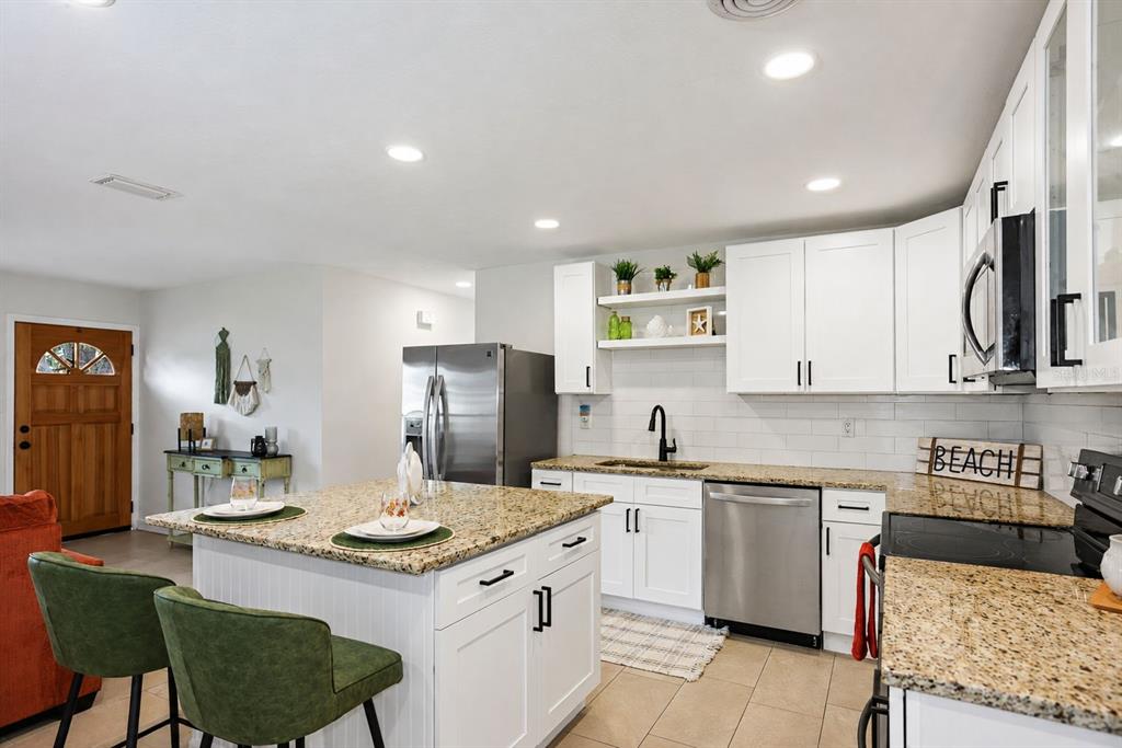 A kitchen features white cabinets, granite countertops, a center island with green stools, and stainless appliances — 482 OAKWOOD DRIVE, DUNEDIN, FL
