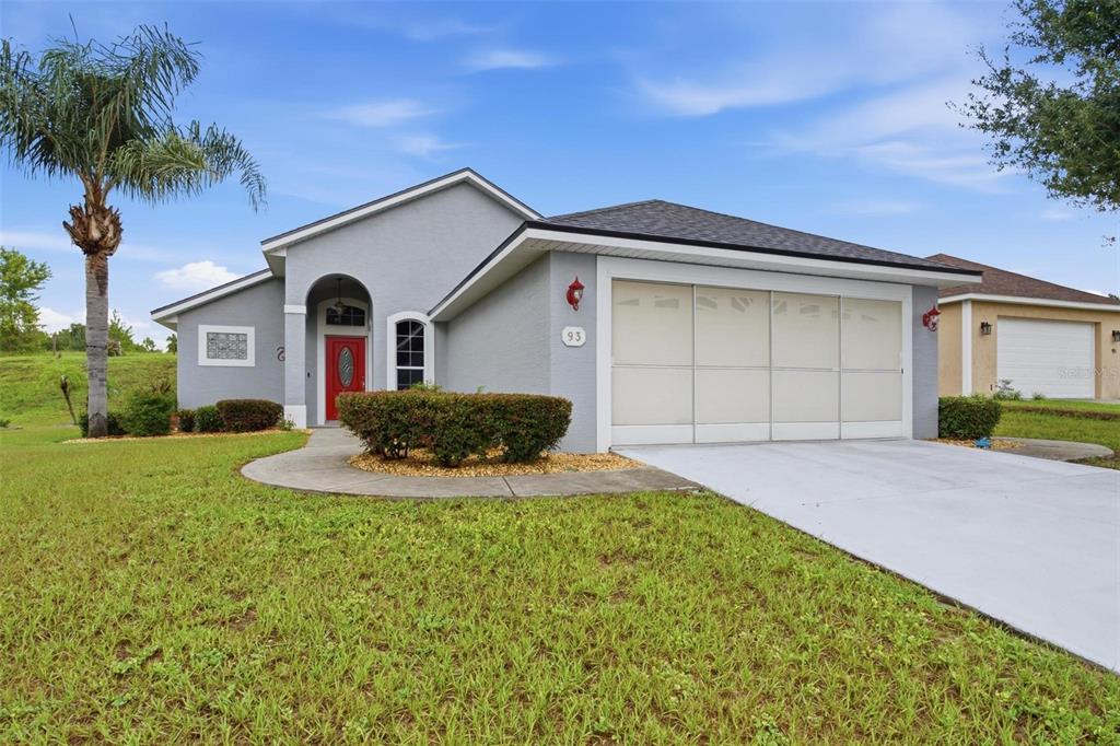A single-story house with a gray exterior, a two-car garage, and an American flag — 93 FAIRWAY CIRCLE, UMATILLA, FL
