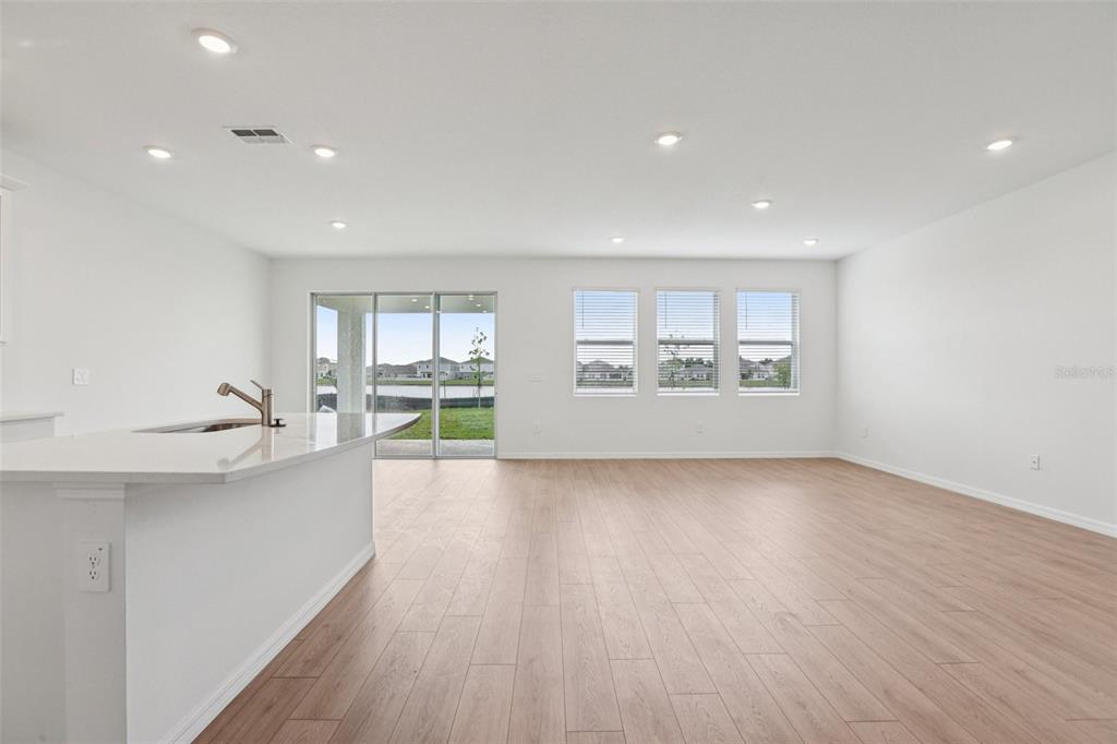 An open-concept kitchen and living area with light wood flooring and sliding glass doors — 5392 CLOUDBERRY, LAKELAND, FL