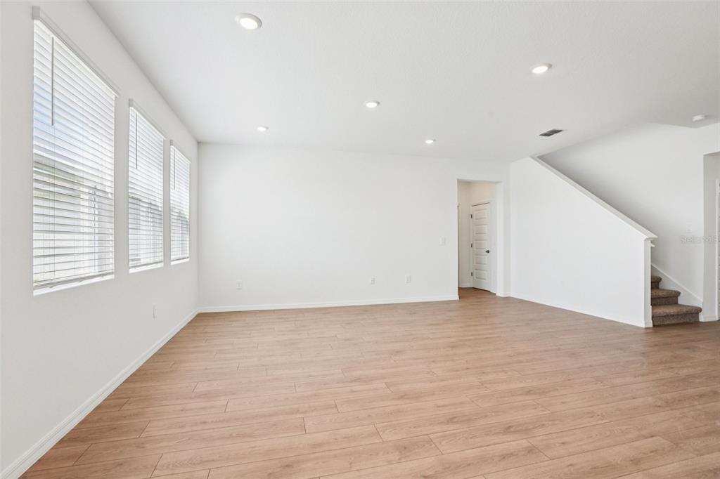An empty living room features light wood-look flooring, white walls, recessed lighting, and large windows — 5392 CLOUDBERRY, LAKELAND, FL