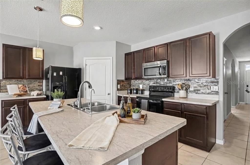 A kitchen features dark wood cabinets, a large island with a sink, and tile flooring — 911 WATERVILLE DR, AUBURNDALE, FL