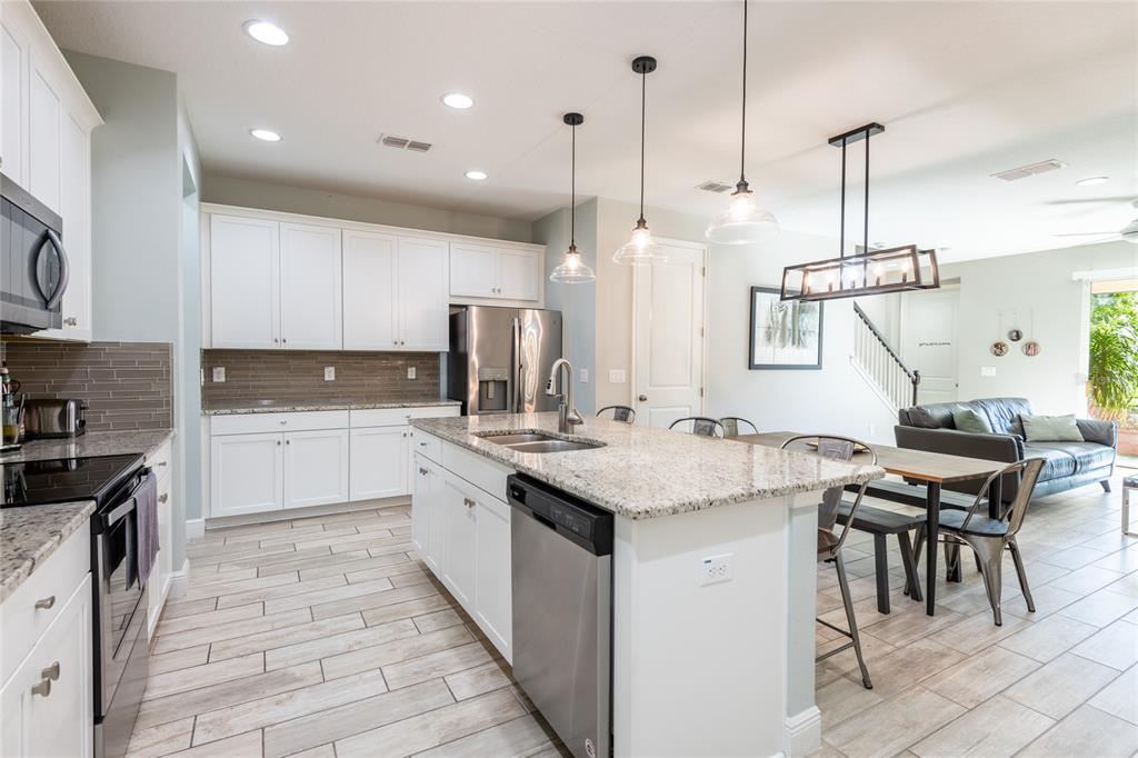 A kitchen features white cabinets, granite countertops, stainless steel appliances, and an island with seating — 17847 ALTHEA BLUE PLACE, LUTZ, FL