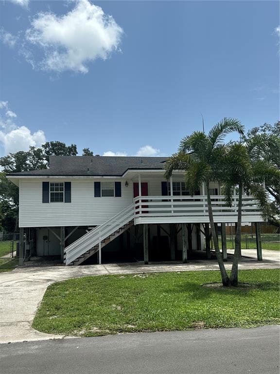 A white elevated house with a front deck, stairs, and a palm tree in the yard — 12055 MURRAY AVENUE, LARGO, FL