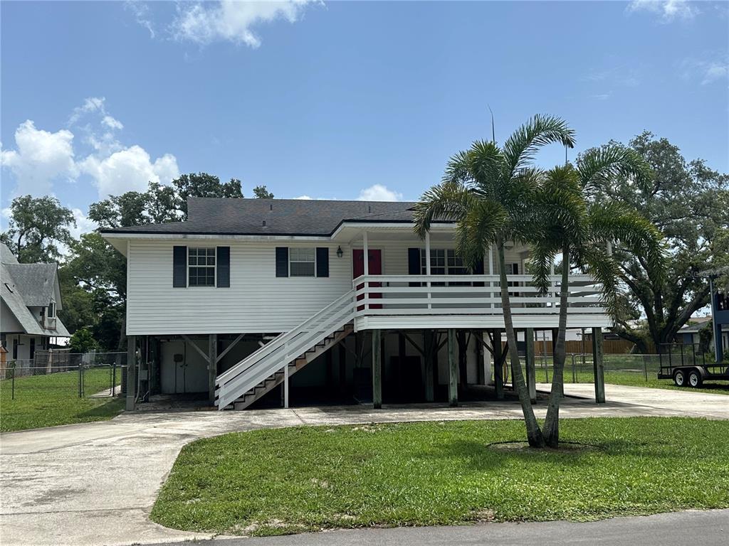 A white elevated house with a front porch, stairs, and a palm tree in the yard — 12055 MURRAY AVENUE, LARGO, FL