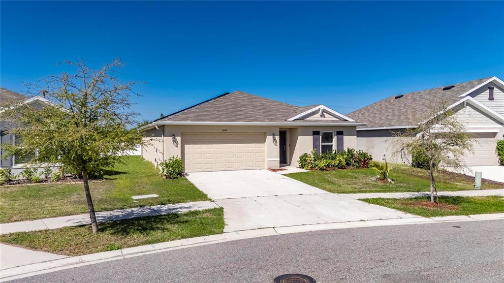 A single-story suburban house with a tan exterior, a two-car garage, and a concrete driveway — 1324 OCEAN SPRAY DRIVE, RUSKIN, FL