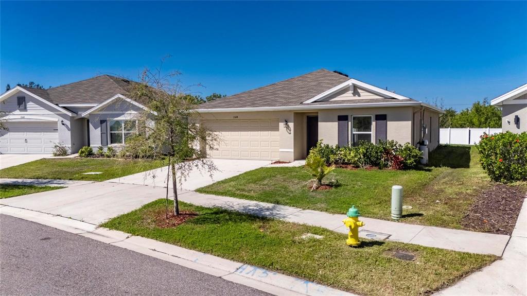 A single-story suburban house with a beige exterior, a two-car garage, and a fire hydrant — 1324 OCEAN SPRAY DRIVE, RUSKIN, FL