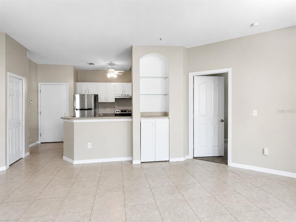 An open-concept living area features tiled floors, a kitchen with white cabinets, and built-in shelving — 2603 MAITLAND CROSSING WAY UNIT 101, ORLANDO, FL
