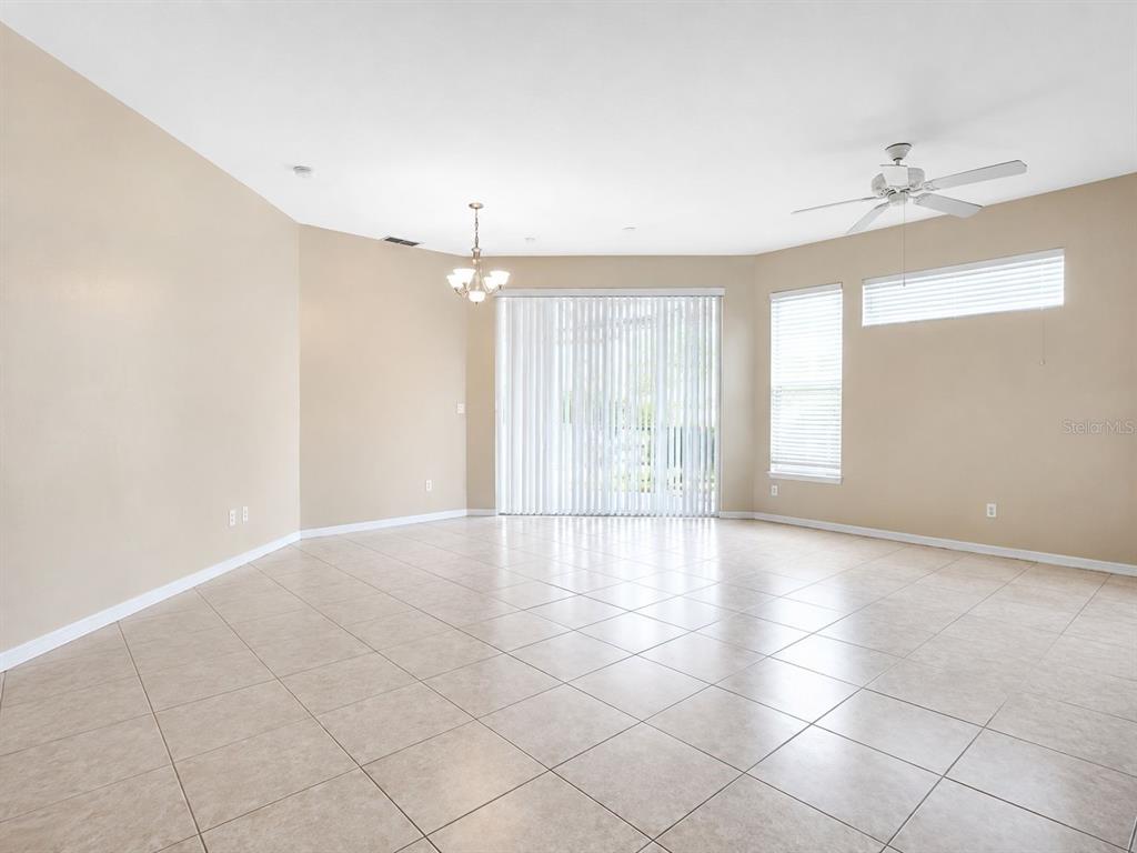 A spacious, empty room features light-colored tile flooring, beige walls, a ceiling fan, and sliding doors — 2603 MAITLAND CROSSING WAY UNIT 101, ORLANDO, FL
