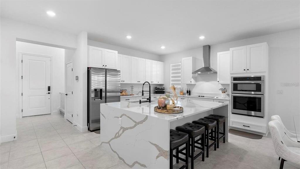 A modern white kitchen features a large marble-topped island with bar seating — 4911 SHADY PINES DRIVE, ST CLOUD, FL