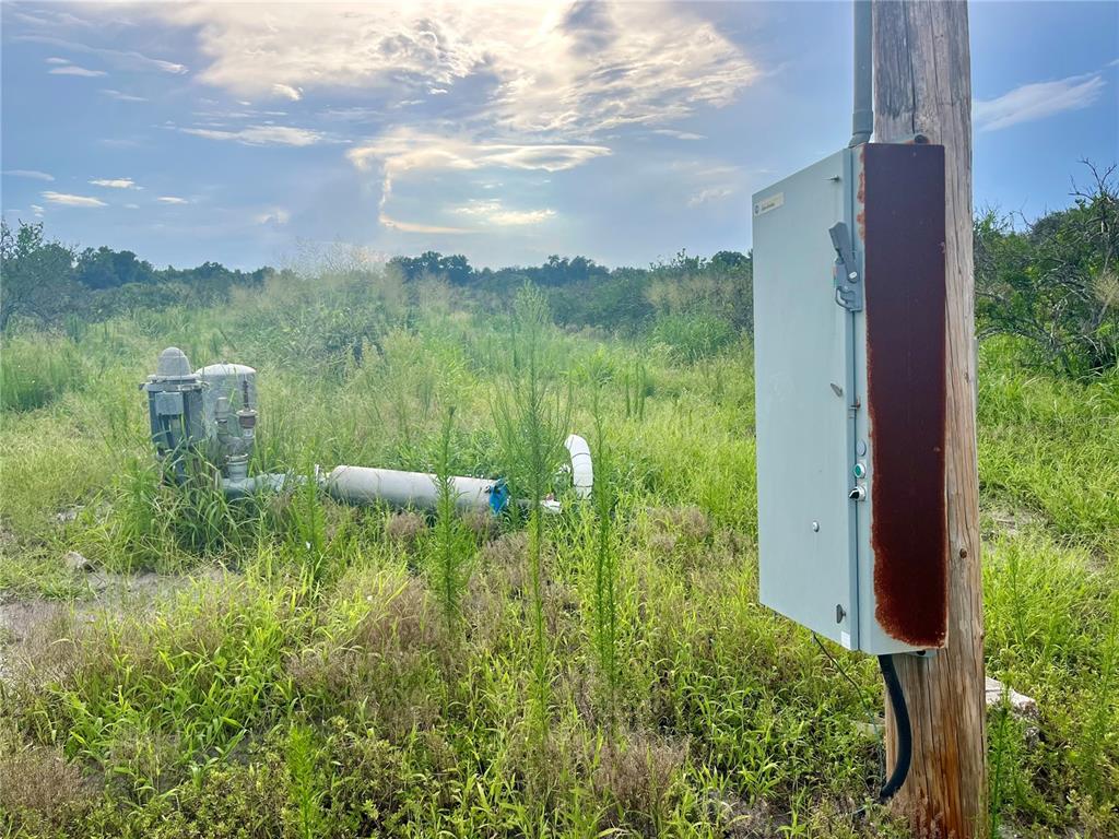 An electrical control box mounted on a wooden pole stands near a water pump — HAYMAN ROAD, WAUCHULA, FL